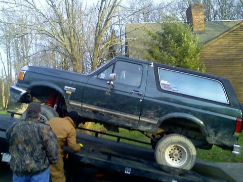 1989 Ford Bronco - A dark green Ford Bronco is being loaded onto a tow truck, with two individuals attending to it.