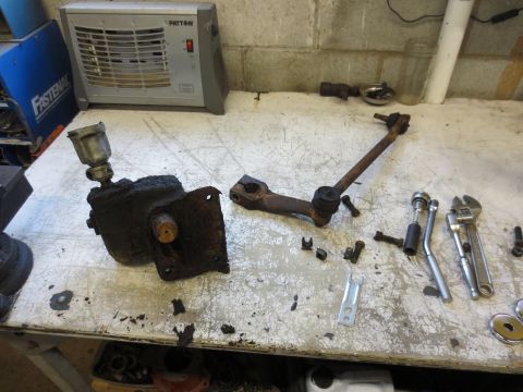 1967 Ford F-250 - Steering gearbox and drag link assembly removed from a vehicle, resting on a workbench with tools.