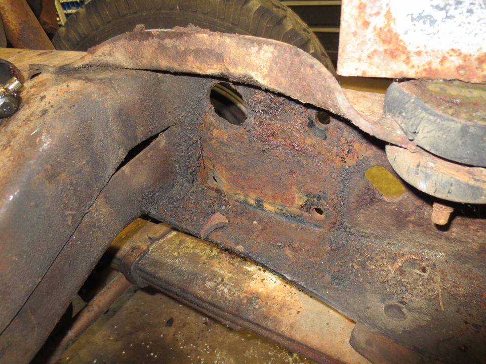 Close-up of heavily rusted truck frame with visible leaf spring and tire in background