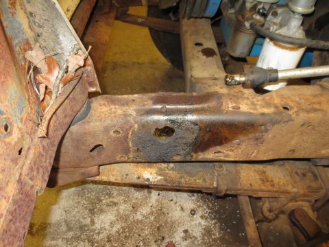 1967 Ford F-250 - Close-up of a heavily rusted 1967 Ford F-250 frame, showing a hole and suspension parts.