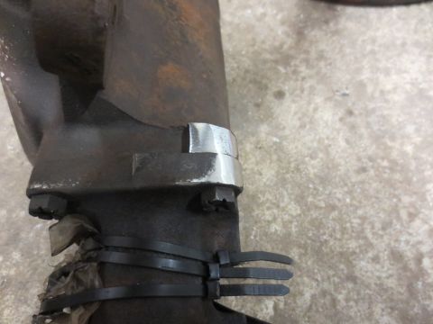 1967 Ford F-250 - A metal clamp is attached to an exhaust manifold with zip ties, showing a close-up view of the part.