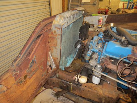1967 Ford F-250 - The engine bay of a 1967 Ford F-250 shows the radiator and blue engine block, with significant rust on the surrounding body panels.
