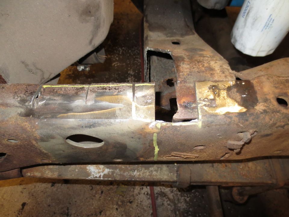 Close-up of a heavily rusted truck frame section with cutouts and weld marks