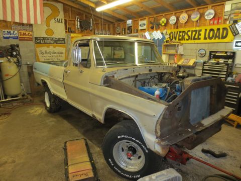 1967 Ford F-250 - A 1967 Ford F-250 pickup truck is undergoing repairs in a cluttered garage, with its hood removed to expose the engine.