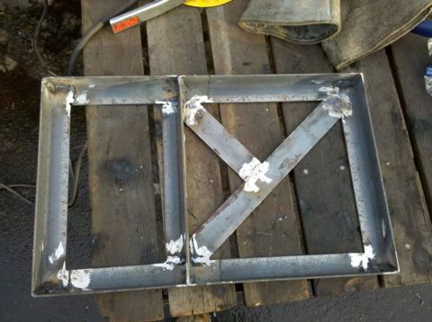1989 Ford Bronco - A custom-fabricated metal frame, likely for a vehicle part, is shown on a wooden workbench.