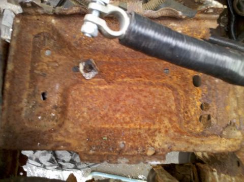 1989 Ford Bronco - Close-up of a heavily rusted metal bracket with a battery terminal and hose attached.