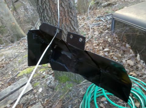 1989 Ford Bronco - Unidentified black metal part mounted on a tree trunk outdoors.