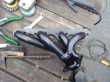 1989 Ford Bronco - An exhaust manifold is shown with various tools, including a grinder and brushes, on a wooden table.