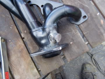 1989 Ford Bronco - A black exhaust manifold is shown on a wooden surface, with visible text from Supermotors.net.