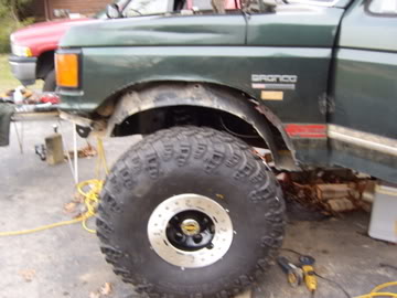 1989 Ford Bronco - This green Ford Bronco is shown with its hood up and a large tire. A red truck is visible in the background.