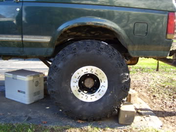 1989 Ford Bronco - The rear side of a green Ford Bronco is shown, with a large tire and a cooler nearby.