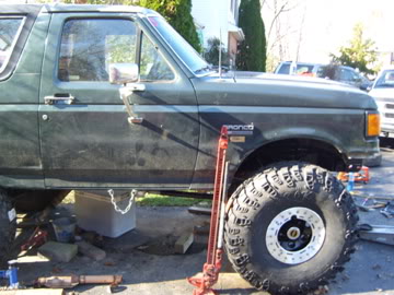 1989 Ford Bronco - This Ford Bronco is elevated on jacks with large off-road tires visible, suggesting maintenance or modification.