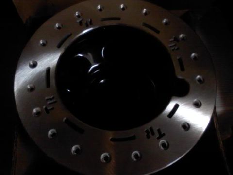 1989 Ford Bronco - Close-up of a metal disc with drilled holes and stamped markings, likely a vehicle part.