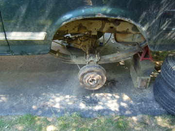 1989 Ford Bronco - The rear axle and suspension of a vehicle are visible, with one wheel removed and the vehicle supported by a jack stand.