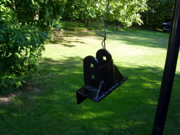 1989 Ford Bronco - A black metal suspension bracket is shown hanging from a hook in a grassy yard with trees in the background.