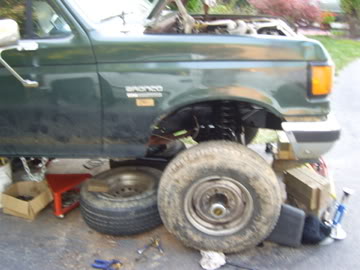 1989 Ford Bronco - Green SUV with hood open and front wheel removed, supported by jack stands.