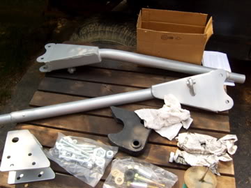 1989 Ford Bronco - Several suspension parts and a box of hardware are arranged on a wooden pallet.