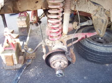 1989 Ford Bronco - Close-up of a vehicle's front suspension and wheel assembly, showing suspension components and a tire. SuperMotors logo visible.