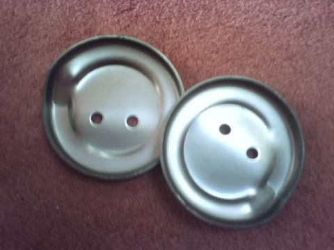 1989 Ford Bronco - Two metal hubcaps, each with two circular holes, are shown against a red fabric background.