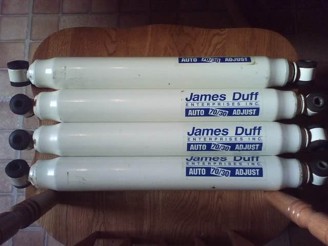 Four white adjustable shock absorbers with James Duff Enterprises Inc. branding