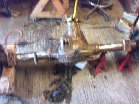 1989 Ford Bronco - A rusty differential axle assembly is supported by red jack stands in a workshop.
