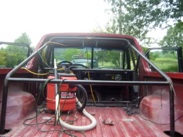 1989 Ford Bronco - Interior view of a red pickup truck with a roll cage and a shop vac in the bed.