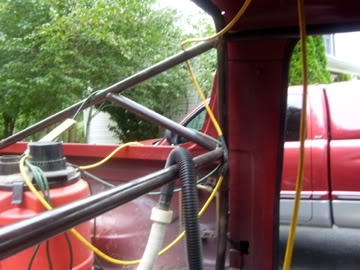 1989 Ford Bronco - Close-up view of a custom roll cage installed inside a red vehicle, with wiring and plumbing components visible.
