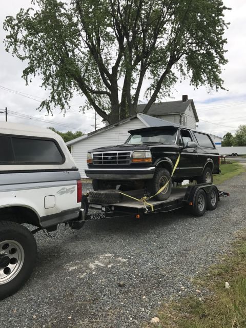 1992 Ford Bronco - A black 1992 Ford Bronco is loaded onto a trailer, being towed by a white pickup truck.