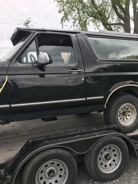 1992 Ford Bronco - A black SUV is loaded onto a trailer, showing its side profile with visible rust on the rear fender.