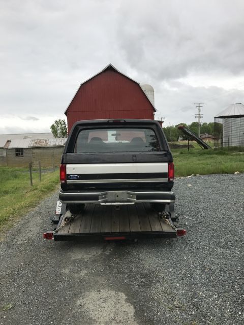 1992 Ford Bronco - A black 1992 Ford Bronco is parked on a trailer in front of a red barn.