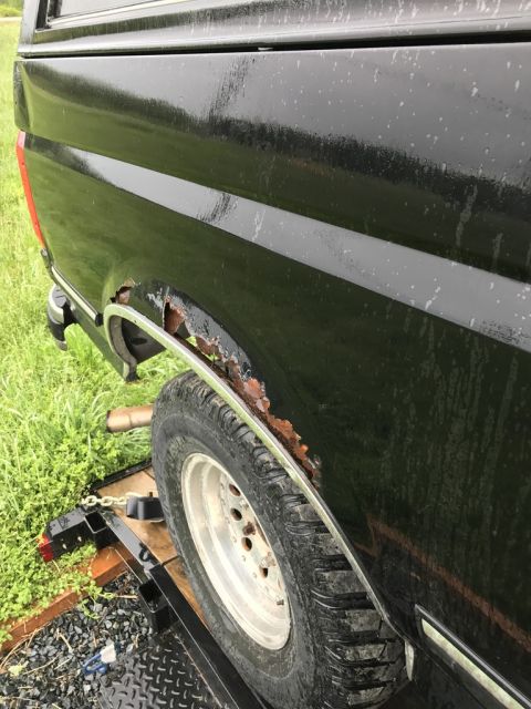 1992 Ford Bronco - The rear fender of a black truck shows significant rust damage around the wheel well.