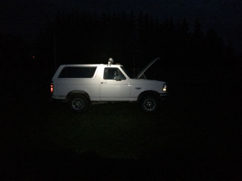 1993 Ford Bronco - A white SUV sits in the dark with its hood open, illuminated by a spotlight.