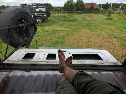 1993 Ford Bronco - Relaxing with feet up in the bed of a vehicle, with a second SUV parked in a grassy field.