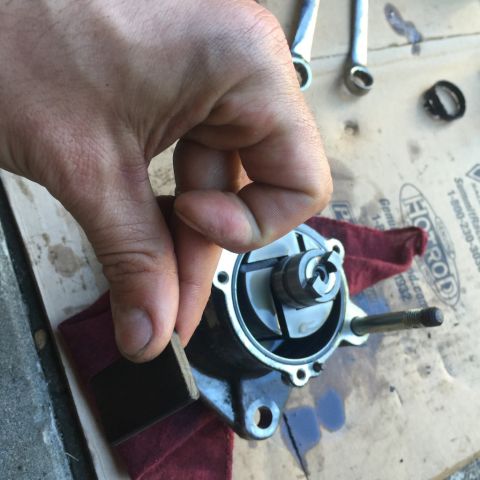 1985 Ford F-350 - A hand holds a vacuum pump part during a repair, with tools and a rag visible on the surface.