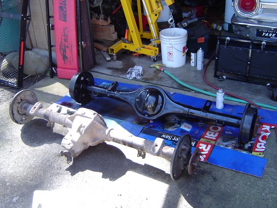 Freshly painted black axle housing beside a bare rusty axle on a driveway