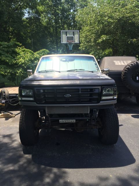 1985 Ford F-350 - This lifted black Ford truck, likely a 1992 model, features aftermarket headlights and a prominent intercooler visible from the front.