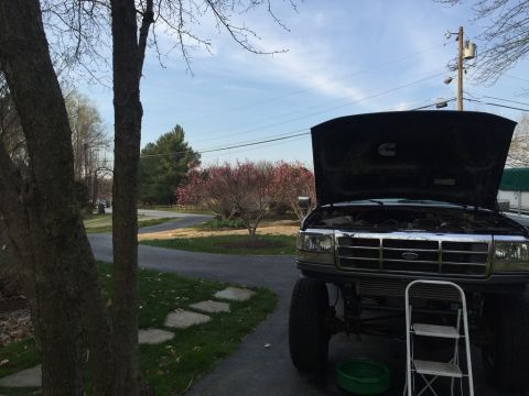 1985 Ford F-350 - A dark Ford truck, likely from the 1990s, sits with its hood open, revealing the engine bay and front grille.