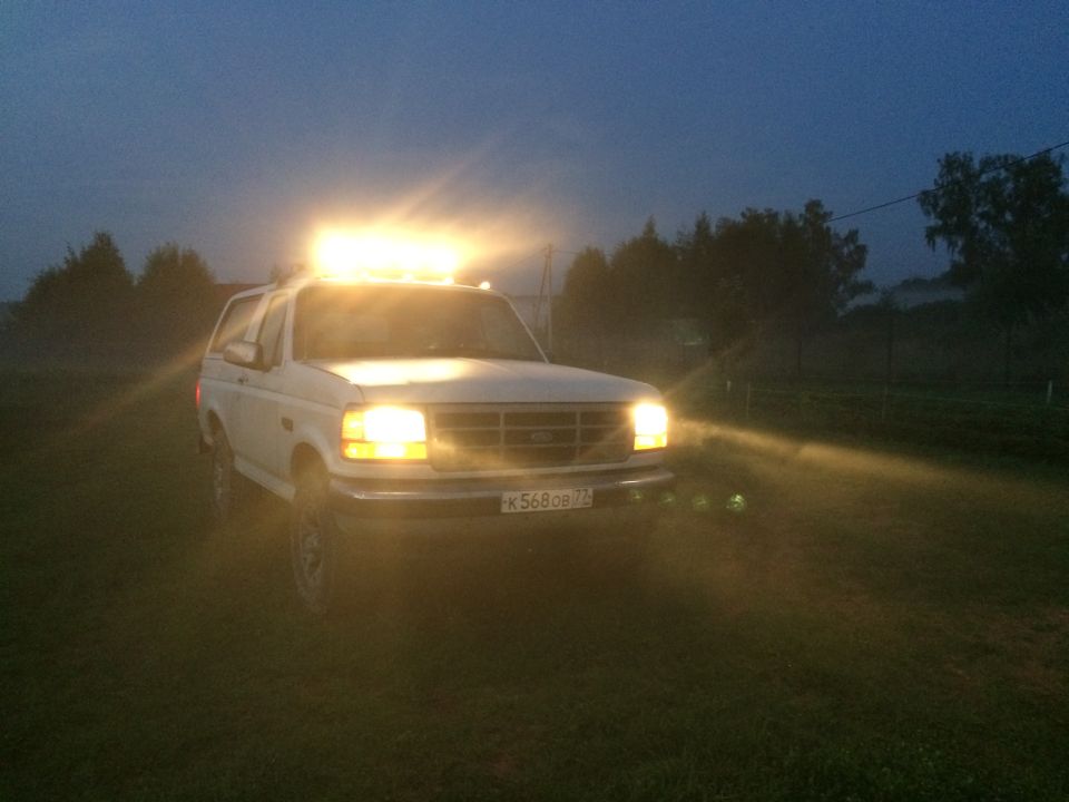 White 1993 Ford Bronco with light bar and headlights on
