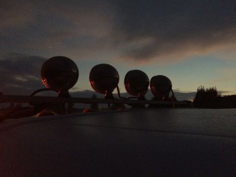 1993 Ford Bronco - Four lights are mounted on a roof rack, silhouetted against a cloudy dusk sky.