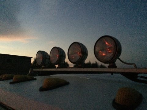 1993 Ford Bronco - Four auxiliary lights are mounted on the roof rack of a vehicle as the sky darkens.