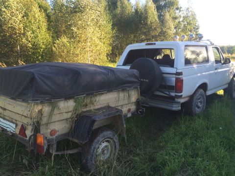 1993 Ford Bronco - A white Ford Bronco is parked in a grassy field, hitched to a trailer covered with a black tarp.