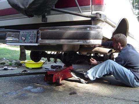 1988 Ford Bronco - A man works on the rear axle of a white and red SUV, supported by a red jack.