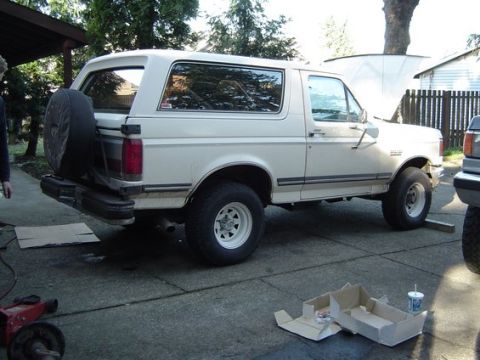 1988 Ford Bronco - Side view of a white 1988 Ford Bronco with a spare tire on the back.