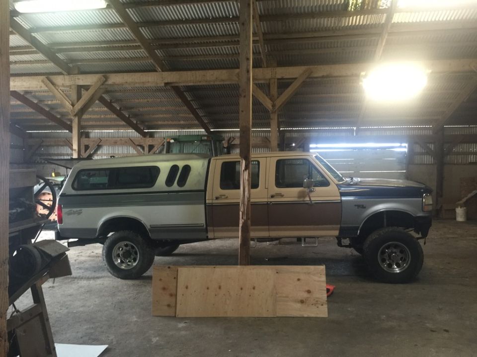 Two-tone Ford F-350 pickup truck with a camper shell, seen from the side in a barn