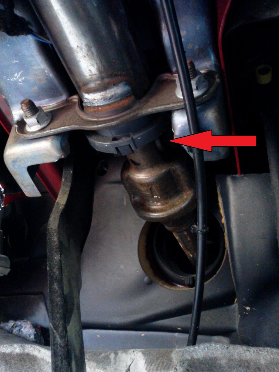 Close-up of a vehicle's steering column linkage with a red arrow pointing to a gray plastic clip