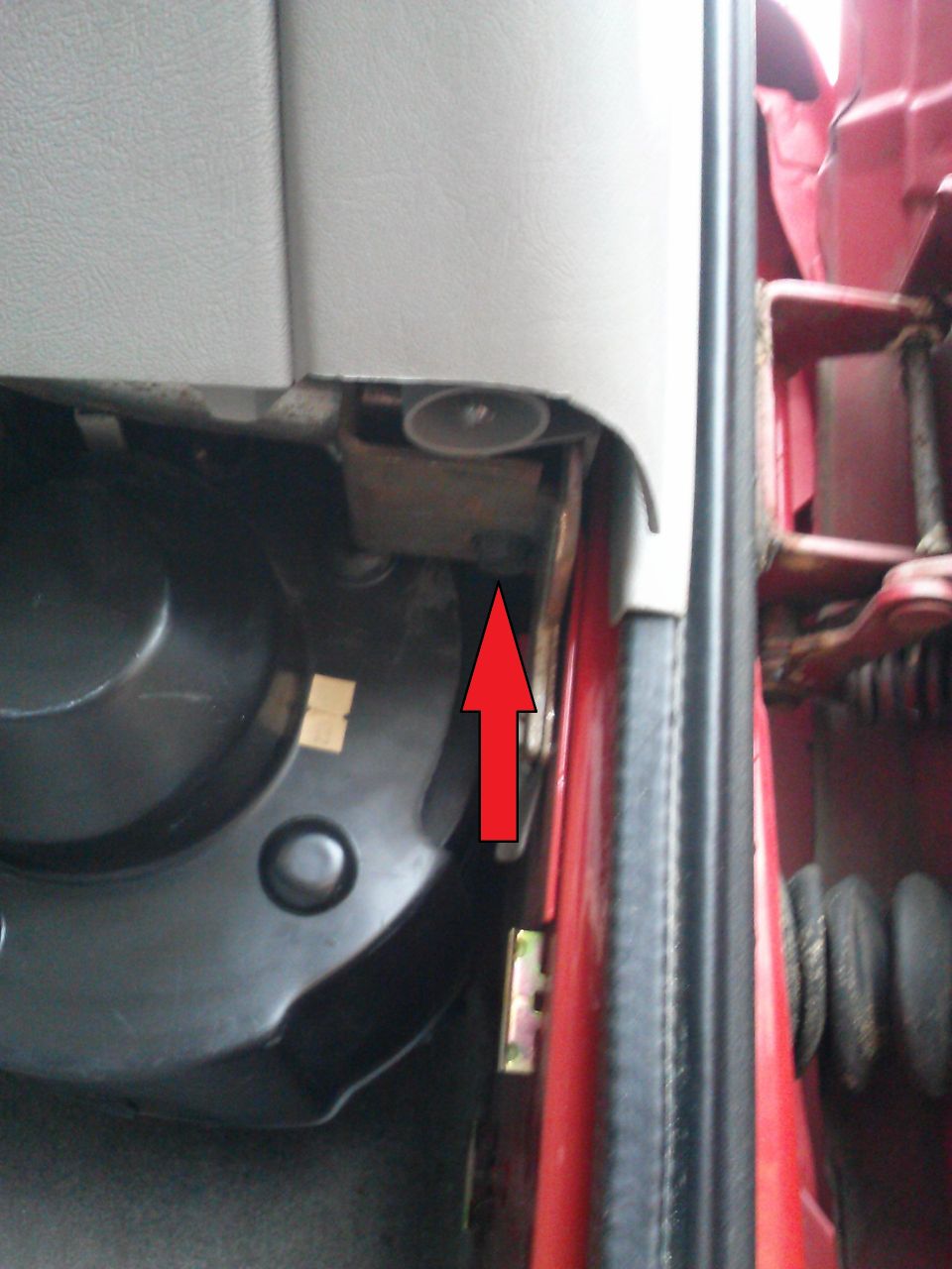 Close-up of interior door jamb with red arrow pointing to a metal bracket