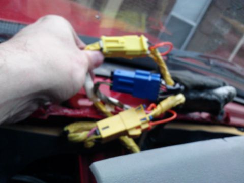 1998 Chevrolet C/K Pickup - A hand manipulates yellow and blue electrical connectors within a vehicle's dashboard wiring harness.