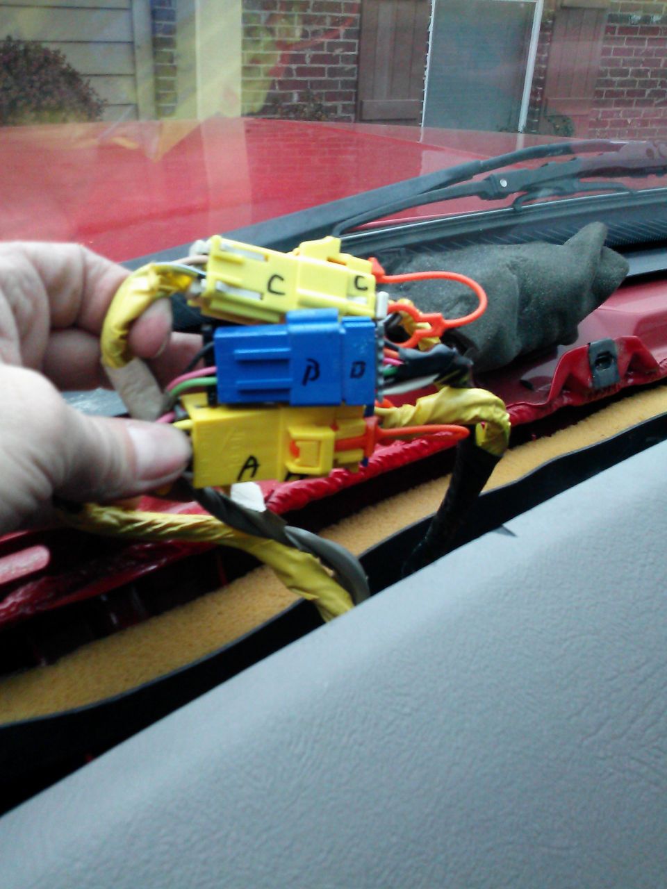 Hand holding yellow and blue wiring harness connectors with labels A, C, and D. Red dashboard visible