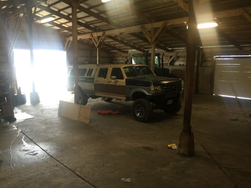 Lifted four-door pickup truck with camper shell inside a barn.