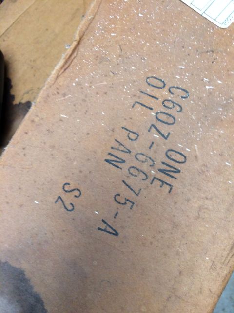 1973 Ford F-100 - A close-up shot shows a part with black lettering that reads "ONE C60Z-6675-A OIL PAN S2". The part appears to be made of a brown, fibrous…